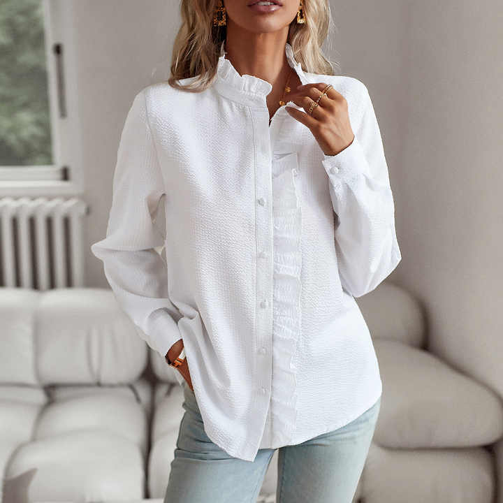 Femme portant une chemise blanche élégante avec col montant, manches longues, posant dans un salon moderne. Mode féminine, tenue décontractée chic.