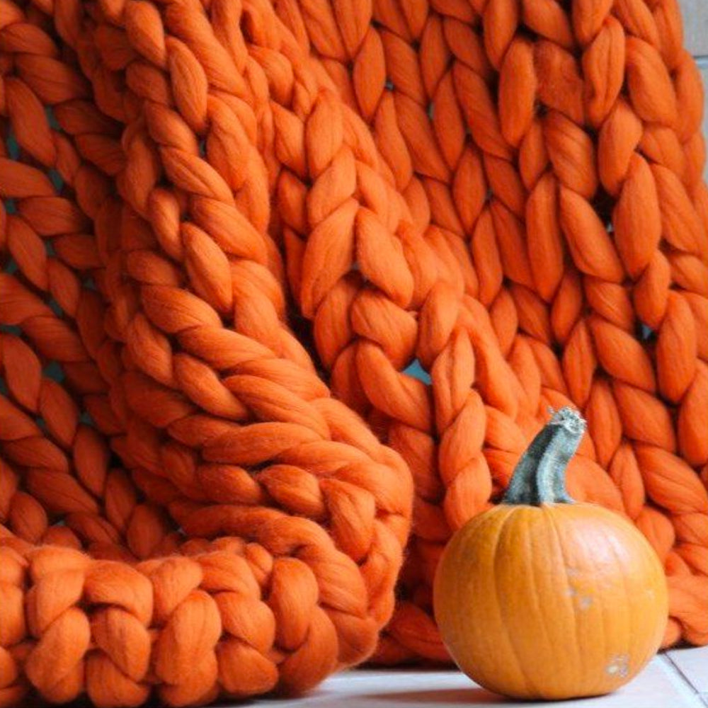 Couverture en tricot épais orange avec une petite citrouille. Décoration automnale, texture douce, ambiance chaleureuse. Accessoire maison tendance.