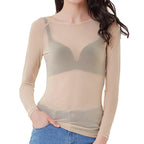 Femme portant un haut transparent beige à manches longues, mettant en valeur un soutien-gorge gris, associée à un jean bleu. Mode féminine tendance.