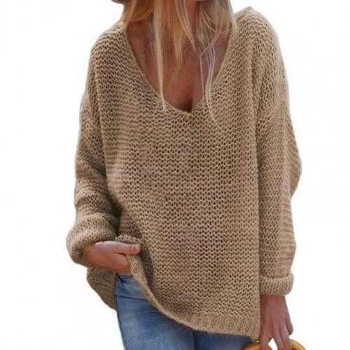 Femme portant un pull en maille beige ample, col en V, manches longues, style décontracté, avec un jean bleu. Mode automne-hiver tendance.