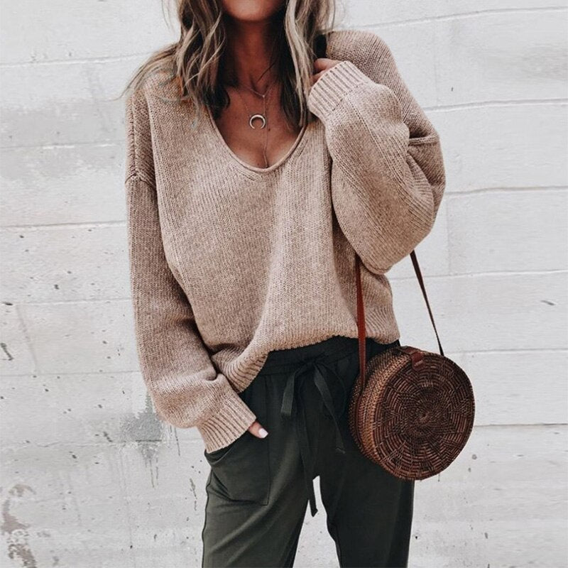 Femme portant un pull en maille beige ample, pantalon vert foncé, et sac rond en osier. Mode automne décontractée, style chic et confortable.