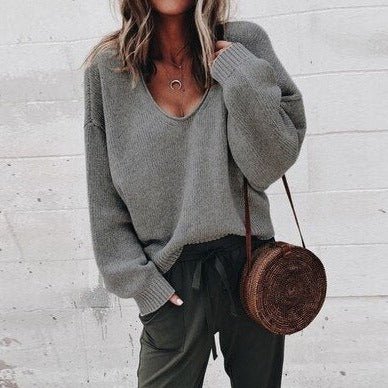 Femme portant un pull gris ample et un pantalon vert, accessoirisée d'un sac rond en osier. Mode décontractée automne, style chic et tendance.