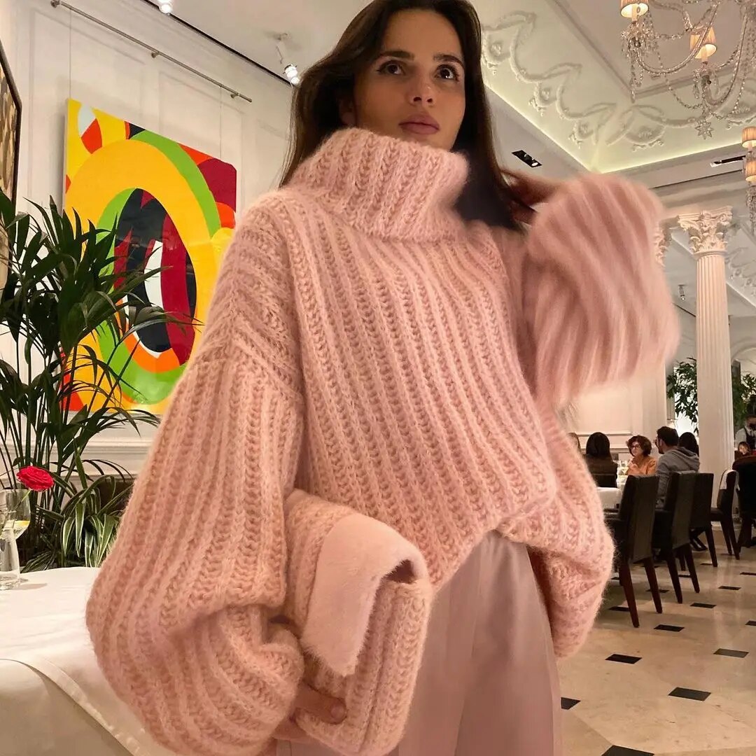 Femme portant un pull en laine rose à col roulé dans un restaurant élégant, art moderne en arrière-plan, ambiance chic et contemporaine.