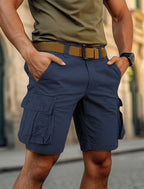 Homme portant un short cargo bleu marine avec ceinture marron, mains dans les poches, debout en extérieur urbain. Mode masculine décontractée.