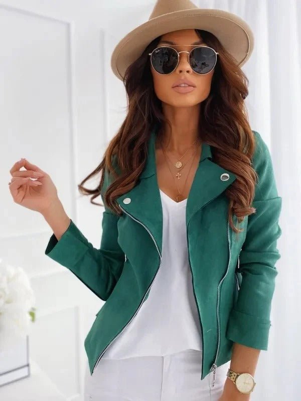 Femme élégante en veste verte, chapeau beige et lunettes de soleil, posant dans un intérieur lumineux. Mode féminine, style chic et moderne.