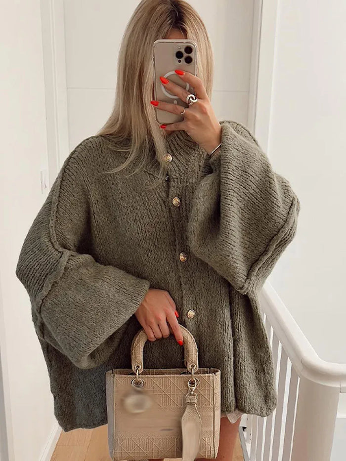 Femme portant un manteau en laine oversize vert avec boutons dorés, tenant un sac à main beige texturé. Mode automne, style chic et tendance.