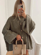 Femme portant un manteau en laine oversize vert avec boutons dorés, tenant un sac à main beige texturé. Mode automne, style chic et tendance.