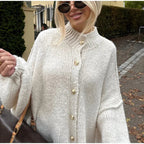 Femme portant un pull en laine blanc avec boutons dorés, lunettes de soleil noires, sac à main marron, style automnal chic, mode féminine tendance.