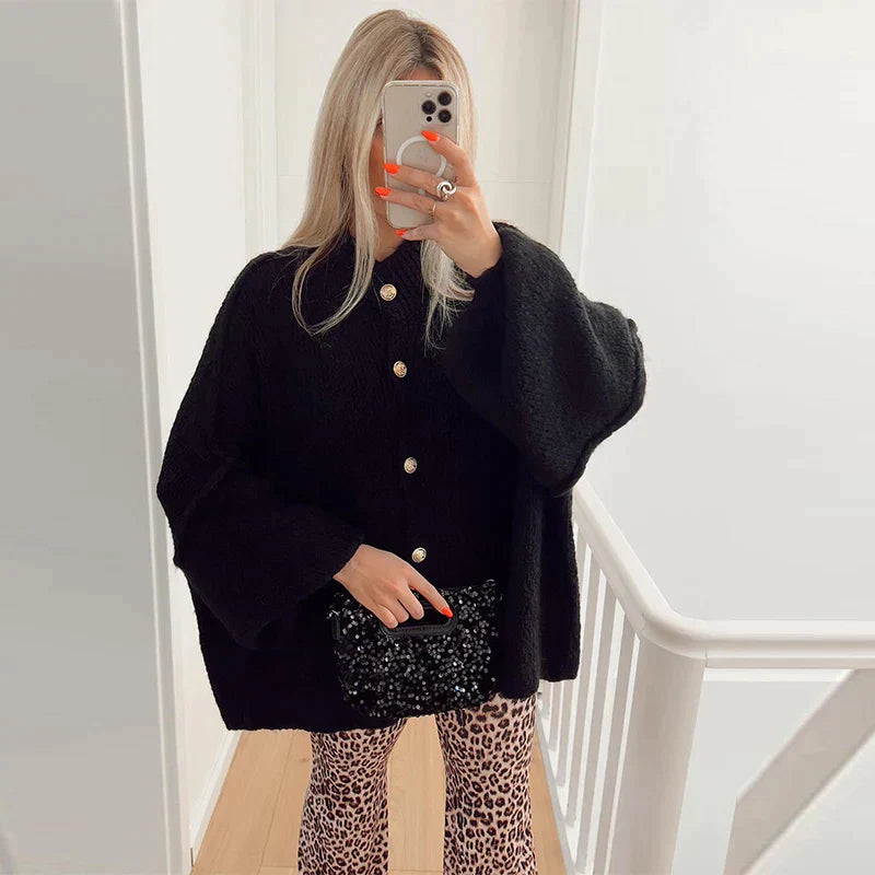Femme prenant un selfie, portant un manteau noir oversize avec boutons dorés, leggings imprimé léopard, tenant un sac à main noir. Mode automne chic.