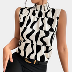 Haut sans manches noir et blanc à motifs géométriques, col montant plissé, porté avec un pantalon noir. Mode féminine élégante et moderne.