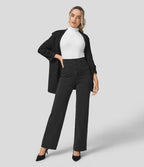 Femme en tenue professionnelle chic, portant un blazer noir, un col roulé blanc et un pantalon taille haute noir, posant sur fond gris.