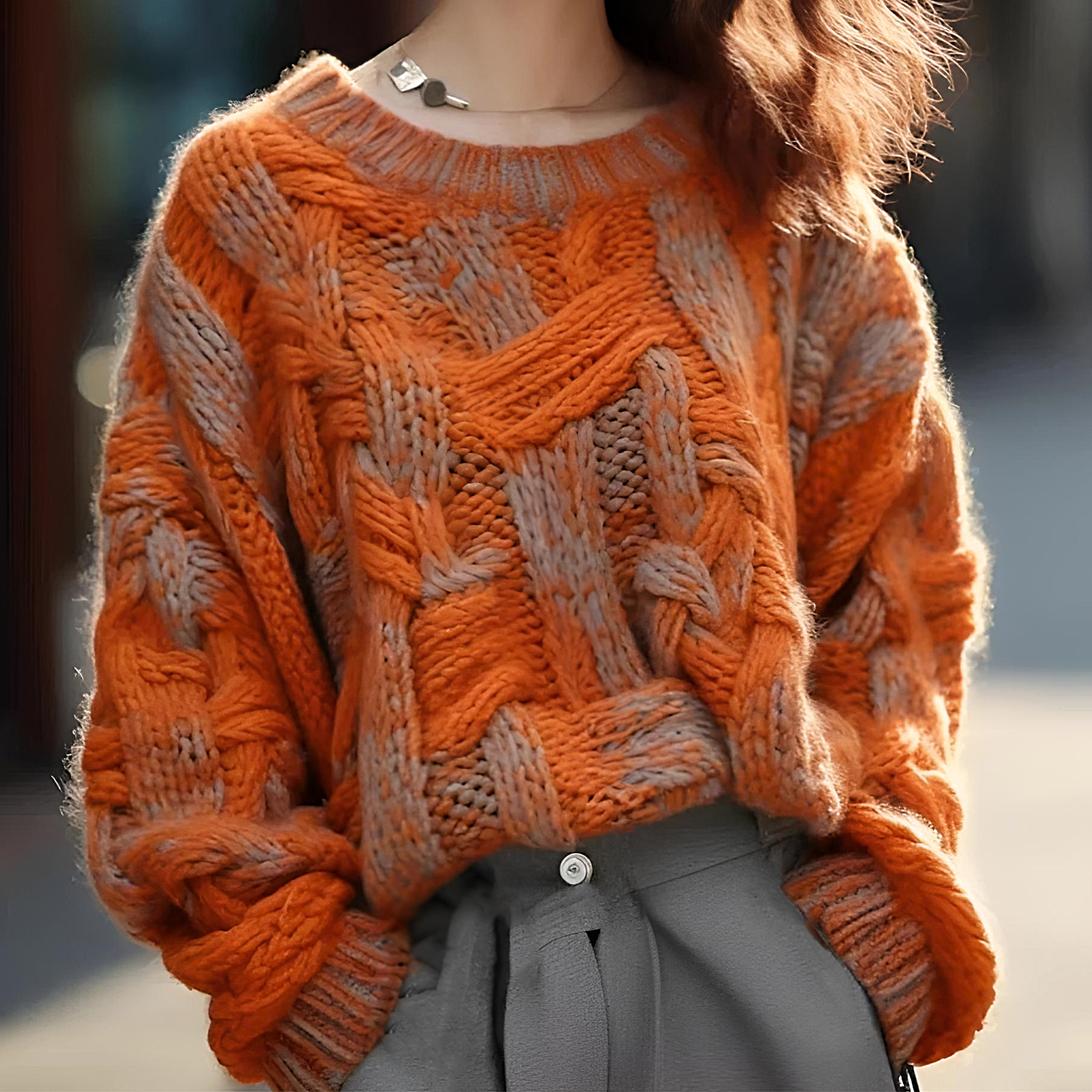 Femme portant un pull en laine orange à motifs torsadés, style automne-hiver, mode décontractée, avec pantalon gris.